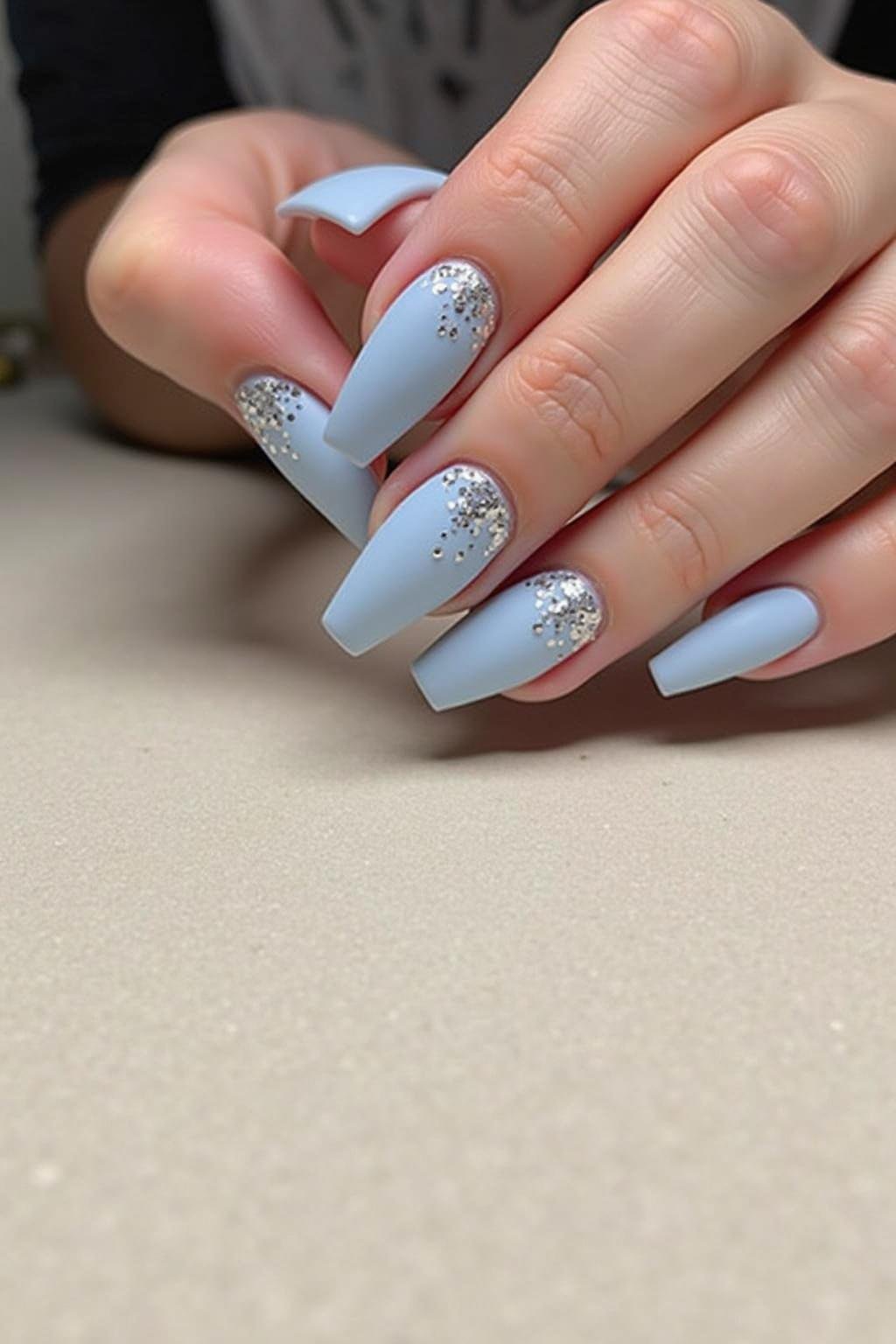 Manicure with matte light blue nails and silver glitter detail, displaying a trendy and elegant style