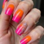 Woman's hand showcasing trendy bright summer coffin nails with neon pink and orange gradient, glitter details, and shiny finish