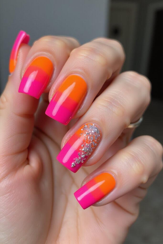 Woman's hand showcasing trendy bright summer coffin nails with neon pink and orange gradient, glitter details, and shiny finish