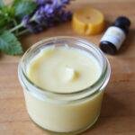 Homemade headache relief balm in a glass jar with lavender, peppermint, and beeswax on a wooden surface
