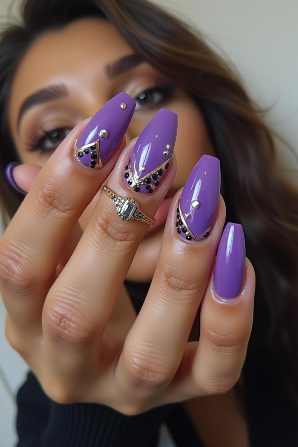 Model's hand with stylish purple acrylic nails featuring geometric patterns and metallic accents