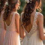 A diverse group of bridesmaids with elegantly styled curly hairstyles, adorned with delicate hair accessories, smiling and standing together in a softly lit bridal setting.