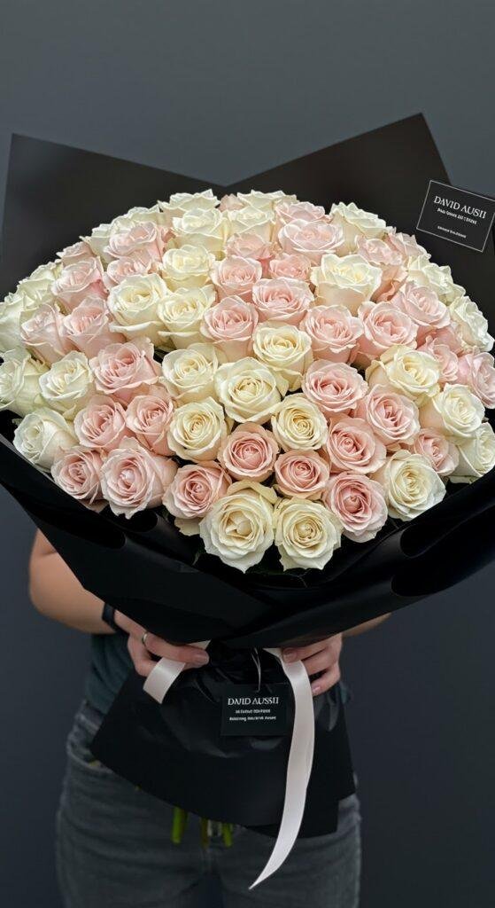 A high-resolution image of an exceptionally large, dense bouquet of luxurious David Austin garden roses in shades of ivory and blush, wrapped in layers of premium black paper, filling the entire frame with elegance and opulence.