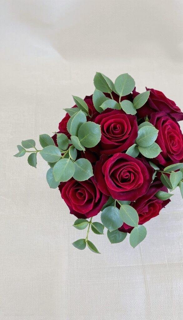A vibrant wedding bouquet featuring deep red roses intertwined with fresh eucalyptus leaves, arranged artfully with a soft-focus background of greenery and delicate flowers, highlighting elegance and romance.