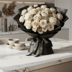 An elegant, welcoming bouquet of neutral-toned flowers wrapped in black paper with a branded ribbon, placed prominently on a kitchen island in a modern, pristine apartment.